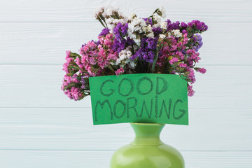 Green vase with statice limonium flowers. White wooden background.