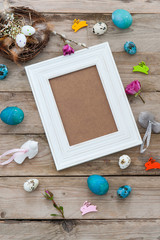 Empty frame on the wooden background with easter decorations around. Flat lay.