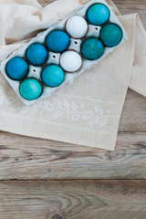 Balsamic blue and green Easter eggs on a textile tablecloth on a wooden tabletop. Empty space for text