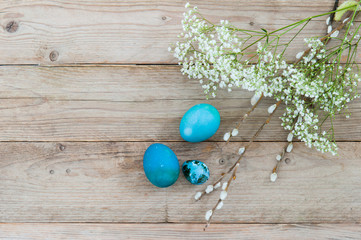 Light wooden background and bright blue Easter eggs with white spring flowers. Space for text. Flat lay
