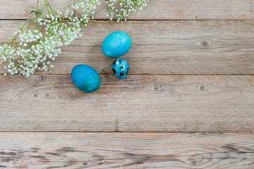 Light wooden background and bright blue Easter eggs with flowers. Empty place for text