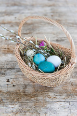 Wicker basket with blue painted Easter eggs on a wooden background