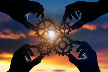 gears in the hands of people on the background of the evening sky. the mechanism of teamwork.
