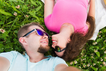 Love, romantic and tenderness concept - Close up selfie of a young and attractive couple laying down on green grass, top view
