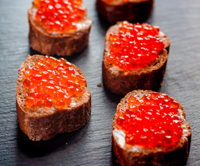 Red caviar on bread on slate background.