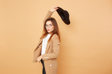 Charming stylish brunette girl with long hair in glasses and a black hat over her head dressed in...