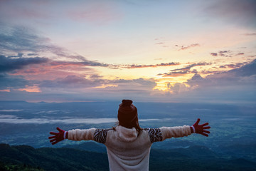 Obraz premium Woman tourist in a sweater dress outstretched arms, happy while watching the beautiful nature landscape of the forest and mountain during the sunrise at Phu Thap Boek Viewpoint Phetchabun, Thailand