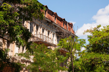 Obraz premium Old historic stone house on the yard with trees around. Old city buildings before and after restavration. Ancient windows, roofs, balconies. sculptures, walls South, summer 