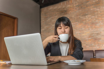 Asian businesswoman drinking coffee and working on laptop