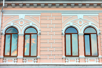 Two windows with brown wooden frame on a background of the pink- white stone wall