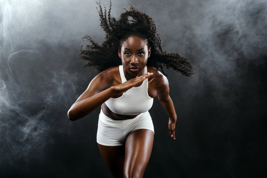 Strong athletic black skin woman sprinter, running on background with smoke wearing in the sportswear. Fitness and sport motivation. Runner concept with copy space.