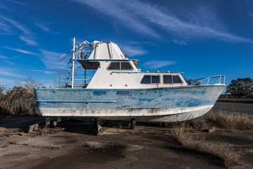 Side view of an abandoned small yacht with faded paint on blocks