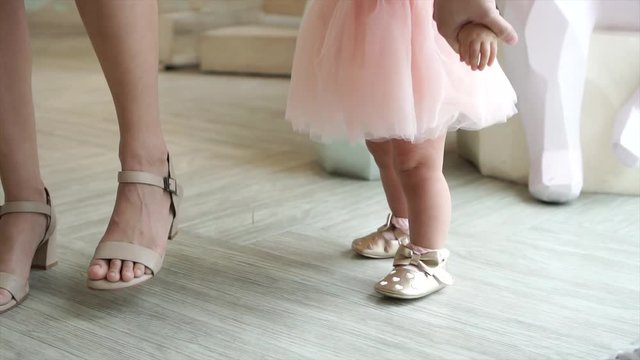 Feet of toddler baby taking first steps with mother help at special event like wedding or birthday party