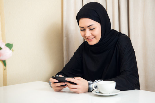 Pretty modern Arabic woman playing on smart phone at home
