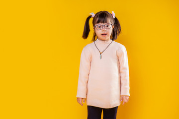 Curious little girl with down syndrome posing against orange wall