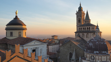 Fototapeta na wymiar Bergamo, Italy. The old town. Aerial view of the Basilica of Santa Maria Maggiore and the dome of the cathedral during the sunset. In the background the Po plain