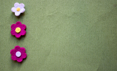 Garden felt flowers over green background. Blank space for text. 