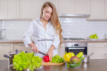 Beautiful girl in a white shirt prepares vegetables in the kitchen