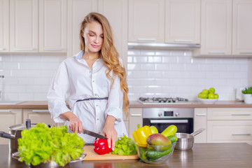 Beautiful girl in a white shirt prepares vegetables in the kitchen