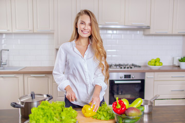 Beautiful girl in a white shirt prepares vegetables in the kitchen