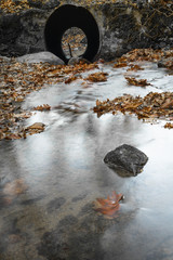 view through water tunnel tube in fall scenery in forest with flowing river in long exposure 