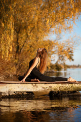 Young woman practicing yoga exercise at quiet pier in autumn park