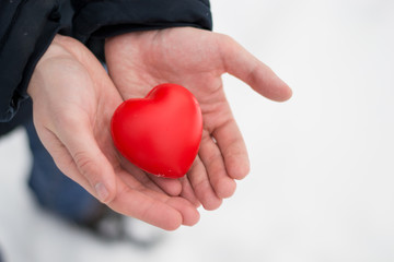 Fototapeta premium Close up red heart in male hands in winter sunny day. Surprise for Valentine's day. I love you. Copy space. Holiday background.