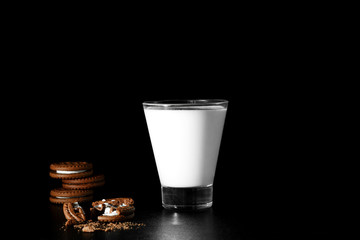 Glass of milk and chocolate cookies on black background