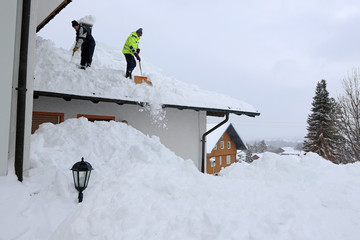 Zwei Männer schaufeln hohen, schweren Schnee von einem Hausdach