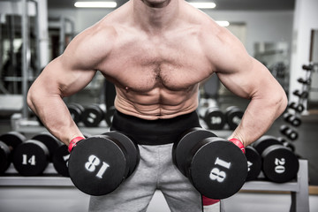 Young sportive man working with dumbbell in gym