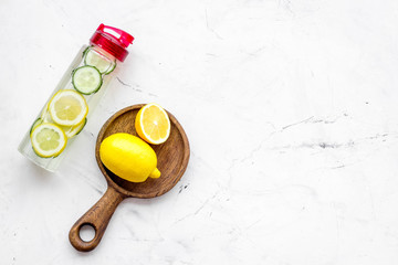 Obraz na płótnie Canvas Detox infused water with slices of lemon and cucumber in bottle on white stone background top view copy space