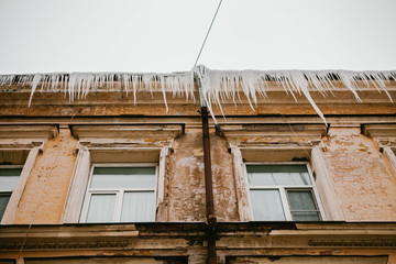 Icicles hang from the roof of a wooden house in the countryside, on a frosty cloudy day.
