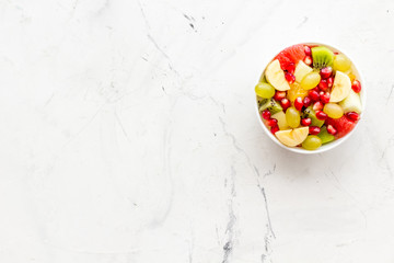 Fruit diet concept. Fruit salad with apple, kiwi and pomegranate in bowl on white stone background top view copy space