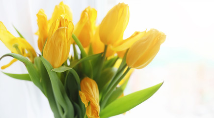 Fototapeta premium A bouquet of red tulips in a vase on the windowsill. A gift for a woman's day from red tulip flowers. Beautiful red flowers in a vase by window.