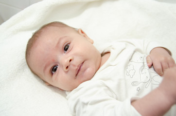 Cute tree months old baby boy dressed in white body looking at the camera while laying on the baby changer