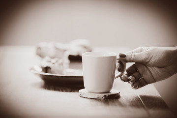 Female hand holding cup near pate with eaten cake and spoon on wooden table. Side view . Image in sepia color style