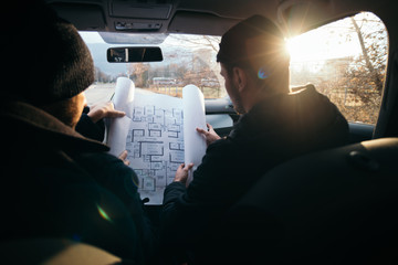 Two violent robbers sitting in a car looking at a blueprint of the building they want to rob while...
