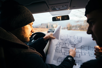 Two violent robbers sitting in a car looking at a blueprint of the building they want to rob while...
