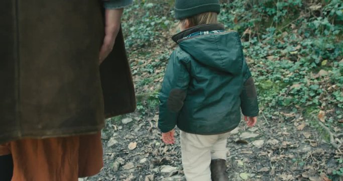 Little toddler walking in forest with mother and grandfather