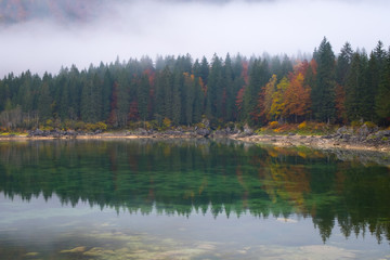Fototapeta na wymiar Reflections of foggy forest on lake Laghi Fusine in autumn