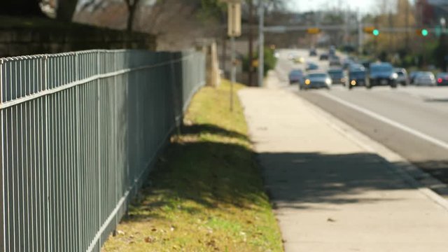 Street scene backplate with foreground in focus and background soft for keying in talent includes green metal picket fence and traffic.