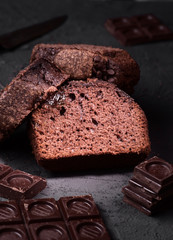 chocolate cake cut with pieces of chocolate and cocoa beans on rough gray background