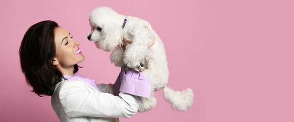 Beautiful woman hugging her lovely white poodle dog puppy on pink happy smiling