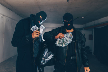 Masked man standing in a garage with money and guns