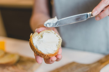 Woman spreading cream cheese on baguette slice on wood board making bruschuetta