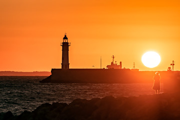 Coastal sunset scene with lighthouse; back light.