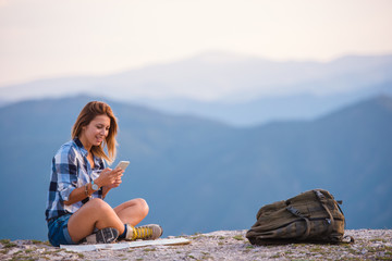 Young lady checking her phone and marveling the view from the top of the world at sunset. Success,...