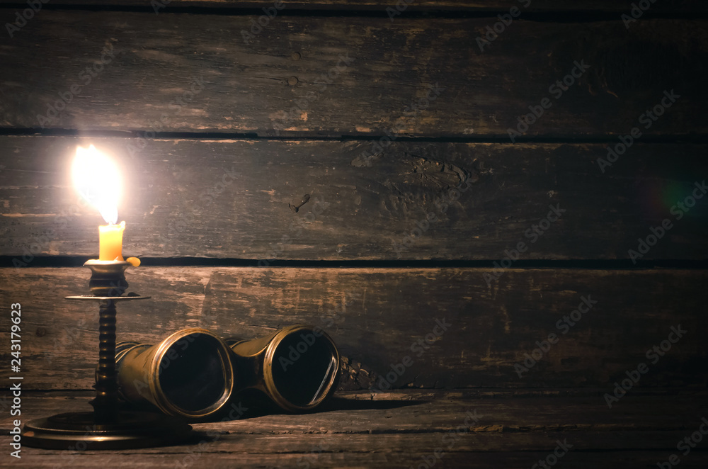 Wall mural binoculars and burning candle on the wooden table background with copy space. travel or adventure co