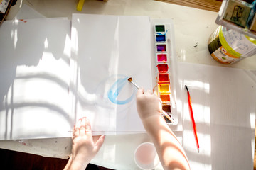 boy is having fun while playing with stamps and tempera paints on wooden work desk producting...