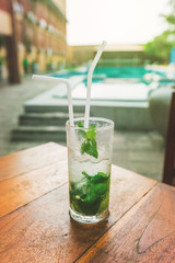 Mojito cocktail with lime and mint in a glass on the table near the swimming pool. Summer sunny day